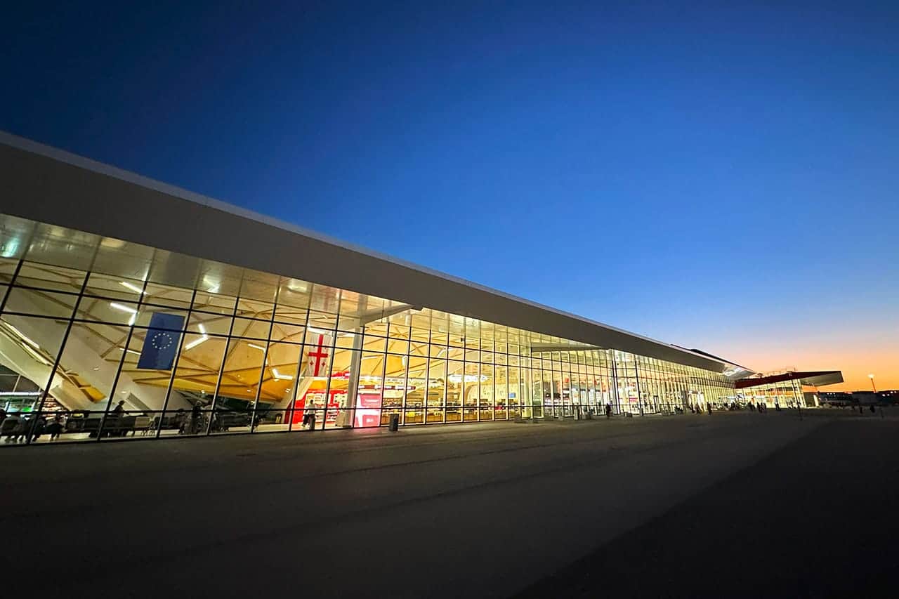 Kutaisi Uluslararası Havalimanı'nın alacakaranlıkta içeriden aydınlatılmış cam terminal binası